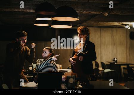 Pregnant businesswoman touching her stomach while working and discussing with her teammates in a positive atmosphere at the office. Stock Photo