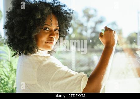 Confident businesswoman looking at camera while writing ideas on a window at the office. Brainstorming and business concept. Stock Photo