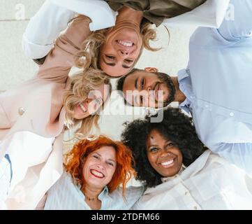 Low angle view of diverse business colleagues embracing and smiling while standing in circle. Business and teamwork concept. Stock Photo