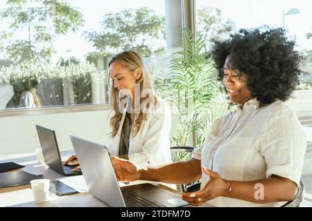 Two female coworkers smiling and having fun while working together in the office. Business concept. Stock Photo