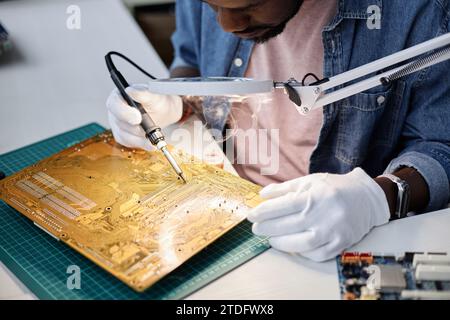 Close up of unrecognizable man repairing circuit board with soldering iron under magnifying glass, copy space Stock Photo