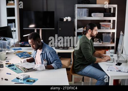 Side view portrait of two people working back to back in computer repair shop, copy space Stock Photo