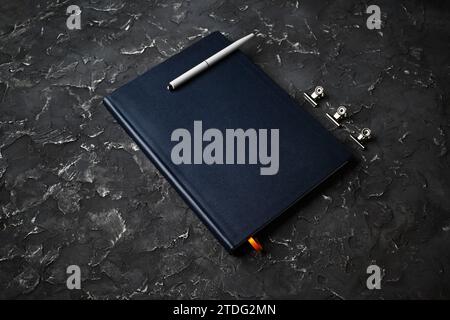 Photo of blank closed notepad and pen on black plaster background. Stock Photo
