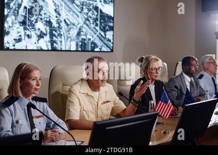 Business people speaking in microphone and discussing difficult situation in the country while sitting at conference Stock Photo