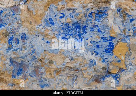 Abstract, detail, pattern of a section of multi-colored, peeling blue and yellow paint layers on an old stone exterior wall of a residence in Jerusale Stock Photo