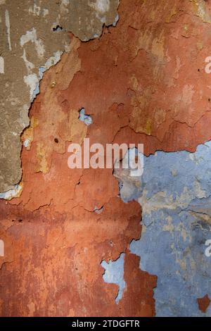 Detail of the colorful, textured exterior wall of an old, painted, peeling stucco building revealing many layers of different colored paint applied ov Stock Photo