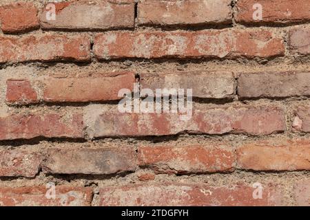 Closeup detail of a section of an old, red brick wall that is worn, chipped and weathered by time. Stock Photo