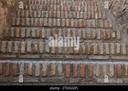 Low-angle view moving up on a staircase in a Spanish fortress made from old, weathered and worn red, clay bricks. Stock Photo