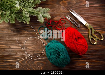knitting needles, yarns and scissors on wooden table decorated with spruce branches Stock Photo