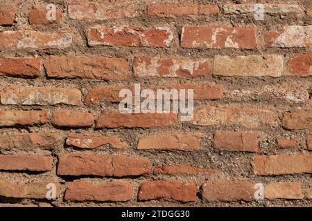 Closeup detail of a section of an old, red brick wall that is worn, chipped and weathered by time. Stock Photo