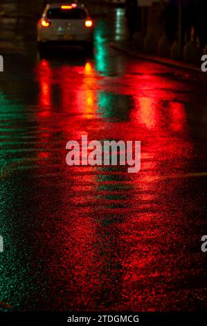 Abstract, wet asphalt road colorfully illuminated at night by red car ...