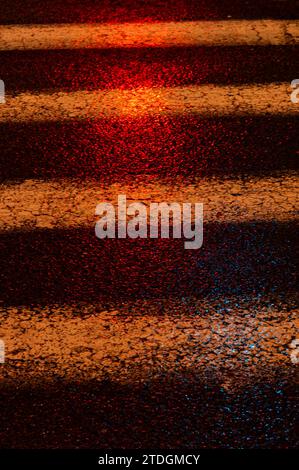 Abstract, textured, cracked section of an asphalt, black crosswalk on a rainy night illuminated by colorful, artificial light. Stock Photo