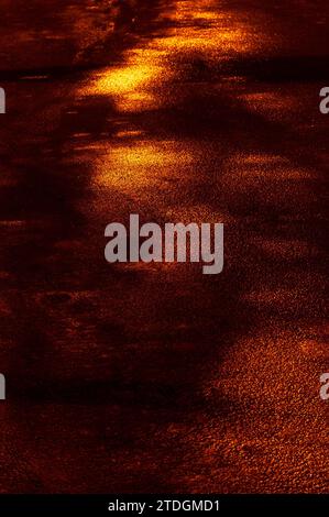 Abstract, textured, cracked section of an asphalt, black road on a rainy night illuminated by colorful, artificial light. Stock Photo