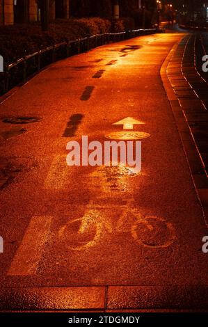 Abstract, textured, cracked section of a bicycle path on a rainy night illuminated by colorful, orange, artificial light. Stock Photo