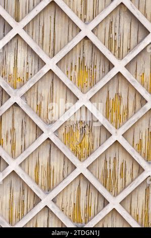 Abstract, white, wooden lattice in a diamond patter overlaid on a weathered, cracked wooden door. Stock Photo