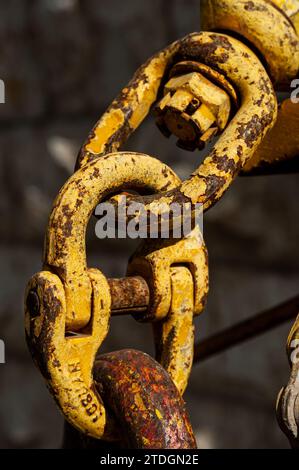 A large, yellow, rusted, textured chain link joining two pieces of road repairing equipment. Stock Photo