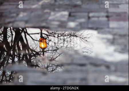 A lone, orange streetlight reflected in a puddle on a sidewalk following a rainstorm in Jerusalem, Israel. Stock Photo