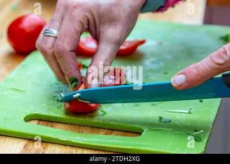 A womans hand holding a knife and chopping a tomato Stock Photo