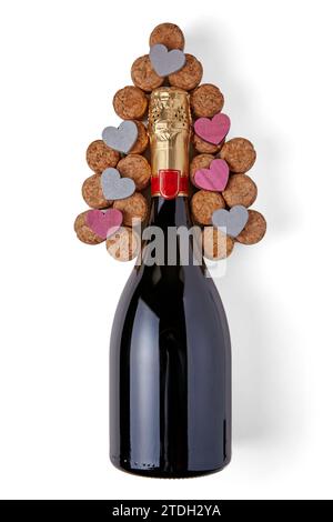 A bottle of sparkling wine surrounded by wine corks laid out in a herringbone shape with decorative wooden hearts Stock Photo