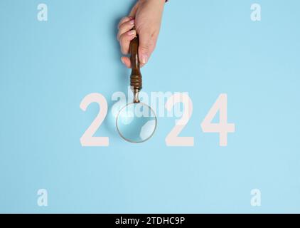 A female hand holds a magnifying glass and the inscription 2024, symbolizing the arrival of the new yea Stock Photo