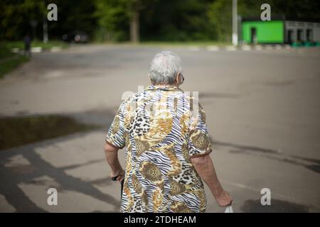 Pensioner walks through city. Grandma on street. Elderly man with walking stick. Woman with bag. Stock Photo