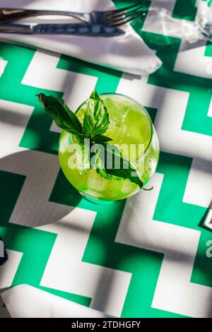 bright green basil lemonade cocktail on restaurant patio table with green and white chevron stripe oilcloth tablecloth Stock Photo
