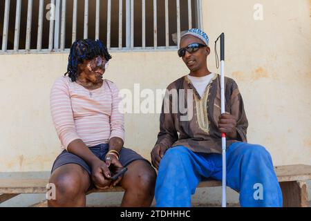 Two smiling African disabled couple sitting on a bench having a conversation. Stock Photo