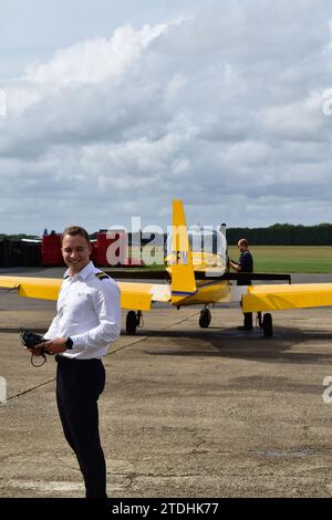 Student pilot with two golden stripes on shoulder epaulette smiling in front of the rear of a yellow Slingsby Firefly at White Waltham Airfield Stock Photo