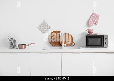 Interior of light kitchen with microwave oven, sink and utensils on white counters Stock Photo