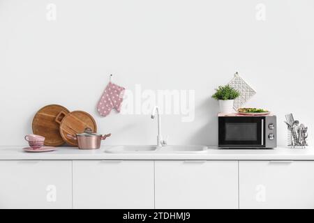 Interior of light kitchen with microwave oven, sink and utensils on white counters Stock Photo