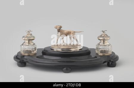Lid ink set with standing dog, fa. Ash. Bonebakker and Son, 1862 There are an oval and a C-shaped floor between the two round openings (the pen box). A black marble lid with a straight, profiled wall fits on the oval floor. On this, a low silver pedestal with plasticly executed plants is also attached to a granulated foundation, with a standing dog with a collar with an open padlock opened on it, completely consed with fine grooves. A silver ribbon with the inscription 1836 - 1873 was mounted on the lid on the lid. Amsterdam silver (metal). glass. marble (rock) grinding There are an oval and a Stock Photo