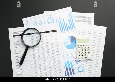 Accounting documents, calculator and magnifying glass on black table, top view Stock Photo