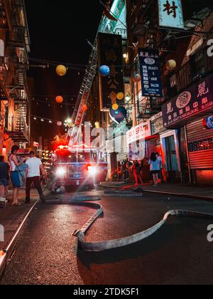 FDNY fire hoses traverse Pell St in Chinatown, New York, while a truck extends its ladder to the roof of an apartment building which was on fire Stock Photo