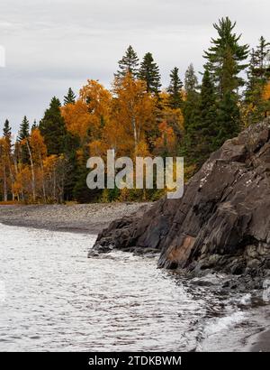 Rocky shoreline of Lake Superior on a stormy day with trees with autumn foliage along the beach. Photographed in Little Two Harbors in Split Rock Ligh Stock Photo