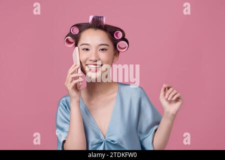 Laughing young woman in hair curlers talking by phone on light background Stock Photo