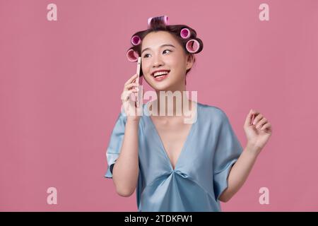 Happy lady talking on phone gossiping with friend, wearing dressing-gown and curlers Stock Photo