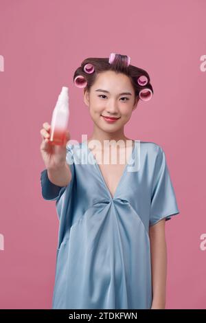 Beautiful young woman holding a bottle in her hand with curlers on her hair Stock Photo