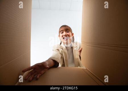 Excited asian woman unpacking, opening carton box and trying to get something, view from the inside Stock Photo