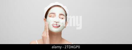 Beautiful woman is getting facial clay mask on white banner background. Stock Photo