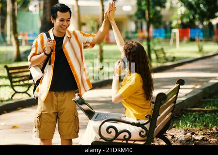 Smiling young man giving high five to friend when meeting her in park Stock Photo