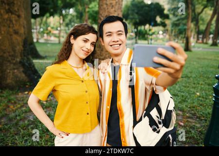 Happy young couple taking selfie on smartphone when walking in park Stock Photo
