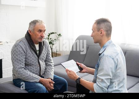 Picture of European doctor talking with elderly male patient and sitting in the studio, isolated on white background Stock Photo