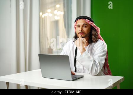 Young Arab man in traditional dress thobe working on computer in office Stock Photo