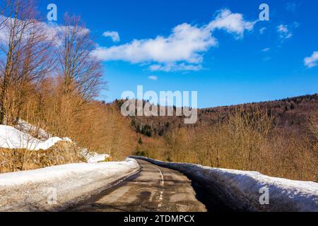 old road pass through snow covered hills. mountainous winter landscape on a sunny day beneath a blue sky with clouds Stock Photo