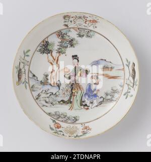 Saucer with two figures in a landscape, a coat of arms and a monogram, c. 1750 - c. 1774 Porcelain dish, painted on the glaze in blue, red, pink, green, yellow, black and gold. On the flat two walking people in a landscape with trees, mountains and a river; The woman on the left has a flower vase in her hands. On the wall an unidentified family crest with three branches against a white background surrounded by curl and flower branches. The helmet sign is also three branches. On the other side on the wall an unreadable monogram with flower branches. Furthermore on the wall a bird on a branch. O Stock Photo