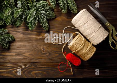scissors, twisted cotton rope and burlap cord on wooden table decorated with spruce branches Stock Photo