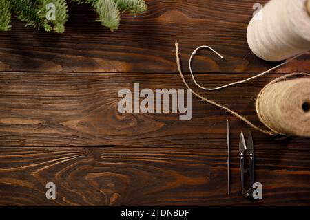Crochet hook, scissors, twisted cotton rope and burlap cord on wooden table decorated with spruce branches Stock Photo