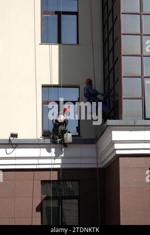 Industrial climbers in protection outfit cleaning window glass on the beige vertical wall closeup Stock Photo