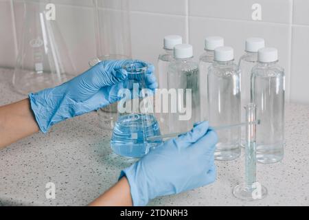 Women hands in the laboratory examines quality of water with a glass tube filled with a blue chemical liquid for research and analysis in the Stock Photo