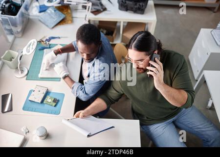 High angle portrait of bearded man speaking by phone in computer repair shop Stock Photo